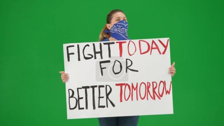Photo for A female activist holds a placard that reads Fight today for a better tomorrow. A woman with her face covered by a scarf on a green screen close up. Protest. Motivation. Rally. Future. Fighting. Rally - Royalty Free Image