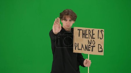 Téléchargez les photos : Un jeune activiste masculin montre un signe qui dit qu'il n'y a pas de planète B et fait un geste d'arrêt d'une main. Un homme dans le studio sur un écran vert de près. Sauver la planète, le réchauffement climatique et le climat - en image libre de droit