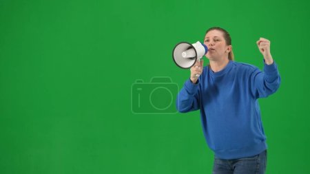 Foto de Activista femenina con el puño levantado gritando en megáfono en el estudio en pantalla verde. Vista frontal de una mujer pro protesta caminando de cerca. Acción de protesta, lucha por los derechos de las mujeres, huelga. Publicidad - Imagen libre de derechos