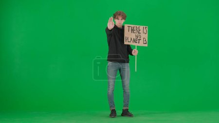 Téléchargez les photos : Un jeune activiste masculin montre un signe qui dit qu'il n'y a pas de planète B et fait un geste d'arrêt d'une main. Un homme dans le studio sur un écran vert. Sauver la planète, le réchauffement climatique et le changement climatique - en image libre de droit