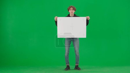 Photo for Male activist holding a large blank placard. Man protesting in studio on green screen - Royalty Free Image