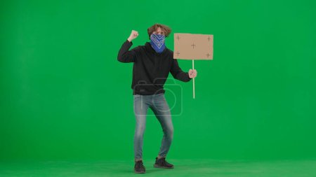 Photo for Male activist with face covered by scarf holding a blank sign. Male protester on green screen. Advertisement, promo, chroma key - Royalty Free Image