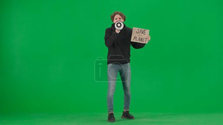 Photo for A man speaks into a megaphone and holds a placard that reads Save Our Planet. Man with a mouthpiece and a poster on a green screen. Save planet, climate changes concept, ecology. Advertising, promo - Royalty Free Image