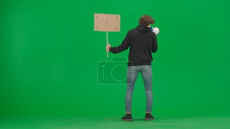 Téléchargez les photos : Homme face à la caméra parlant dans un mégaphone et tenant une pancarte vierge dans sa main. Vue arrière d'un homme avec un embout buccal et une pancarte sur un écran vert. Action de protestation - en image libre de droit