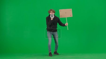Photo for Man speaking into a megaphone and holds a blank placard in his hand. A man with a mouthpiece and placard on a green screen. Protest action, fight for human rights, strike. Advertising, promo, chroma - Royalty Free Image