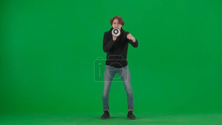 Photo for Male activist with raised fist shouting menacingly into megaphone in studio on green screen. Front view of a pro protest man. Protest action, fight for human rights, strike. Advertising, promo, chroma - Royalty Free Image