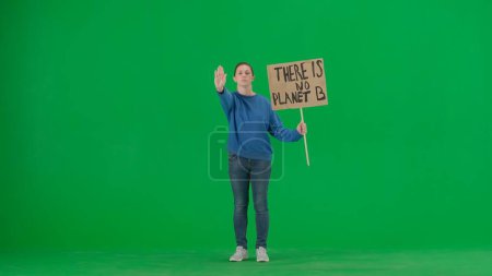 Photo for A young female activist shows a sign that says There is no planet B and makes a stop gesture with one hand. A woman in the studio on a green screen. Save the planet, global warming and climate change - Royalty Free Image
