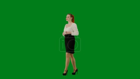 Téléchargez les photos : Femme d'affaires moderne. Portrait d'une jolie fille de bureau sur écran vert chroma. Femme en jupe et chemisier marchant expression souriante, boire du café dans une tasse. Demi-tour. - en image libre de droit