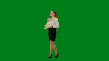 Foto de Mujer de negocios moderna. Retrato de atractiva chica de oficina en croma pantalla verde clave. Mujer en falda y blusa caminando sosteniendo cuaderno y escribiendo ideas, cara enfocada. Media vuelta.. - Imagen libre de derechos