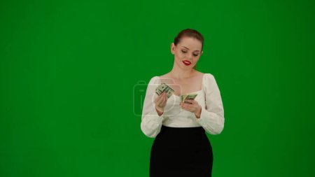 Téléchargez les photos : Femme d'affaires moderne concept de publicité créative. Portrait d'une jolie fille de bureau sur écran vert chroma. Femme en jupe et chemisier debout comptant l'argent, heureux sourire expression du visage. - en image libre de droit