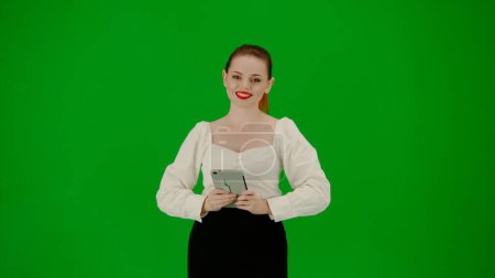 Photo for Modern business woman creative advertisement concept. Portrait of attractive office girl on chroma key green screen. Woman in skirt and blouse talking at camera holding tablet, advertising service. - Royalty Free Image
