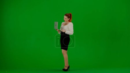 Foto de Mujer de negocios moderna concepto de publicidad creativa. Retrato de atractiva chica de oficina en croma pantalla verde clave. Mujer en falda y blusa sosteniendo portátil y mecanografía, expresión enfocada positiva. - Imagen libre de derechos