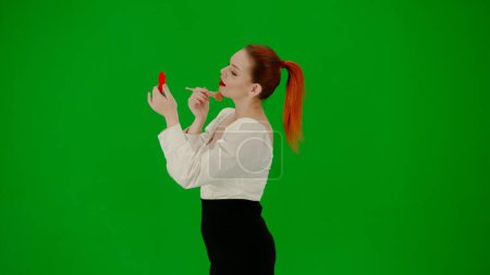 Foto de Mujer de negocios moderna. Retrato de atractiva chica de oficina en croma pantalla verde clave. Una mujer en una blusa y falda de negocios se está empolvando la cara con un cepillo y un espejo. - Imagen libre de derechos