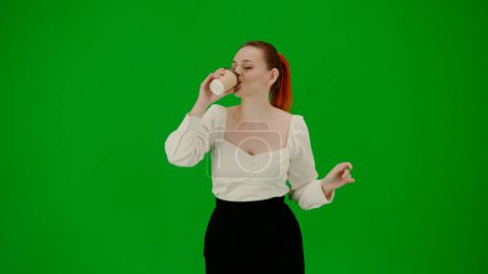 Foto de Mujer de negocios moderna concepto de publicidad creativa. Retrato de atractiva chica de oficina en croma pantalla verde clave. Mujer en falda y blusa sosteniendo papel taza bebiendo café y bailando cutely. - Imagen libre de derechos