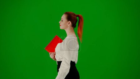 Téléchargez les photos : Femme d'affaires moderne. Portrait d'une jolie fille de bureau sur écran vert chroma. Femme en jupe et chemisier marchant avec dossier en papier et sacs en papier cadeau rouge. Vue latérale. - en image libre de droit