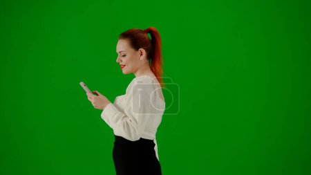 Photo for Modern business woman creative advertisement concept. Portrait of attractive office girl on chroma key green screen. Woman in skirt walking holding gift bags and texting on smartphone. Side view. - Royalty Free Image