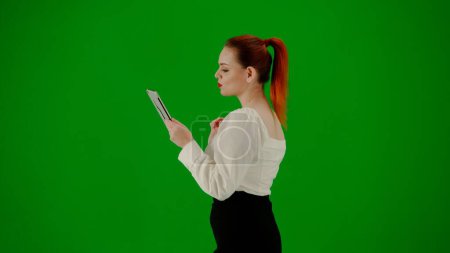 Photo for Modern business woman creative advertisement concept. Portrait of attractive office girl on chroma key green screen. Woman in skirt and blouse walking holding texting on tablet. Side view. - Royalty Free Image