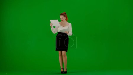 Téléchargez les photos : Femme d'affaires moderne concept de publicité créative. Portrait d'une jolie fille de bureau sur écran vert chroma. Femme en jupe et chemisier lisant des documents, visage confus expression désemparée. - en image libre de droit