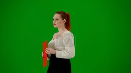 Foto de Mujer de negocios moderna concepto de publicidad creativa. Retrato de atractiva chica de oficina en croma pantalla verde clave. Mujer en falda y blusa caminando sosteniendo carpeta roja. Media vuelta.. - Imagen libre de derechos