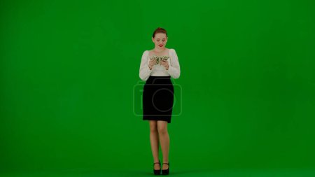 Téléchargez les photos : Femme d'affaires moderne concept de publicité créative. Portrait d'une jolie fille de bureau sur écran vert chroma. Femme en jupe et chemisier debout comptant l'argent, heureux sourire expression du visage. - en image libre de droit