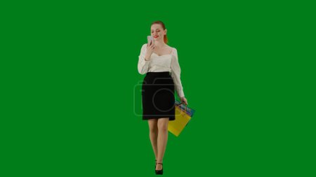 Foto de Mujer de negocios moderna concepto de publicidad creativa. Retrato de atractiva chica de oficina en croma pantalla verde clave. Mujer en falda caminando hablando en el teléfono inteligente por videollamada, expresión feliz. - Imagen libre de derechos
