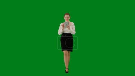 Téléchargez les photos : Femme d'affaires moderne concept de publicité créative. Portrait d'une jolie fille de bureau sur écran vert chroma. Femme en jupe marchant et tenant la tablette, expression positive. - en image libre de droit