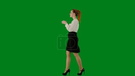 Photo for Modern business woman. Portrait of attractive office girl on chroma key green screen. Woman in skirt and blouse walking smiling expression, drinking coffee from a mug. Side view. - Royalty Free Image