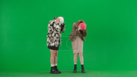 Foto de Dos mujeres con pasamontañas blancas y rosadas se molestaron por una pérdida o malas noticias. Mujeres monstruos en abrigos de piel en el fondo verde del estudio - Imagen libre de derechos