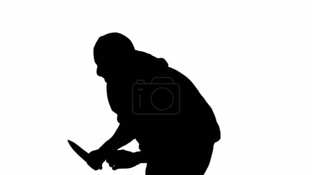 Téléchargez les photos : Silhouette noire de voleur sur fond blanc isolé. Un voleur en sweat à capuche et cagoule marche avec un couteau dans les mains, se préparant à commettre un crime. Demi-tour - en image libre de droit