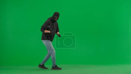 Photo for Robbery and criminal concept. Portrait of thief on chroma key green screen background. Man robber in black balaclava and hoodie holding crowbar in hands - Royalty Free Image