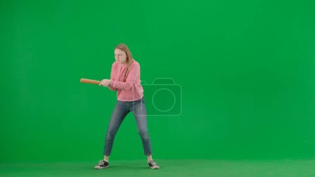 Photo for Robbery and criminal concept. Portrait of victim on chroma key green screen background. Young girl walking alone, scared face expression, holding baseball bat , looking around. - Royalty Free Image