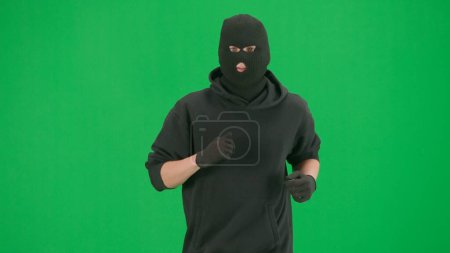 Photo for Robbery and criminal concept. Portrait of thief on chroma key green screen background. Man robber wearing hoodie, jeans and black balaclava, running getting ready for making a crime. - Royalty Free Image