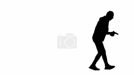 Photo for Black silhouette of thief on isolated white background. Male robber in hoodie and balaclava walking with a gun in his hands, preparing to commit a crime. Side view - Royalty Free Image