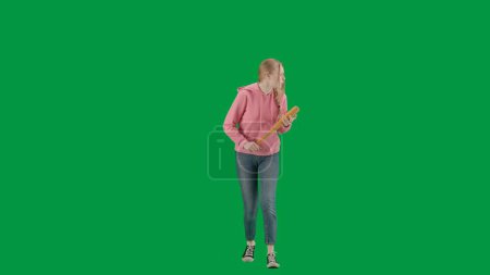 Foto de Robo y concepto criminal. Retrato de la víctima en el fondo de pantalla verde croma clave. Chica joven caminando sola, expresión de cara asustada, sosteniendo bate de béisbol, mirando a su alrededor. - Imagen libre de derechos