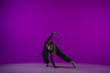 Téléchargez les photos : Danse contemporaine énergique dans la lumière violette studio : jeune fille en vêtements noirs montre grâce et passion pour la danse. Sur toute la longueur. Promo ou commercial - en image libre de droit