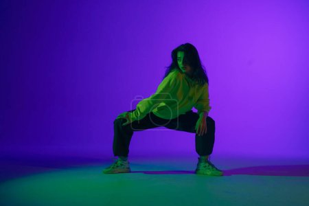 Live jazz-funk performance in the studio: a young stylish girl in casual clothes embodies the rhythm and energy of dance under purple-green light