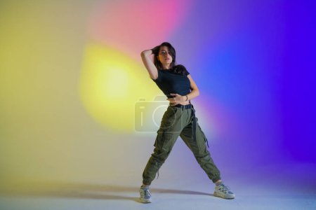 Foto de Mujer joven en ropa negra posando en el estudio con luz de neón azul degradado, amarillo, rosa. Bailarín demuestra elementos de jazz funk estilo danza. Coreografía contemporánea - Imagen libre de derechos
