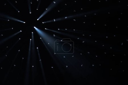 Foto de Los rayos de luz brillante atraviesan agujeros en el fondo negro del estudio. Los rayos atraviesan la oscuridad iluminando el espacio - Imagen libre de derechos