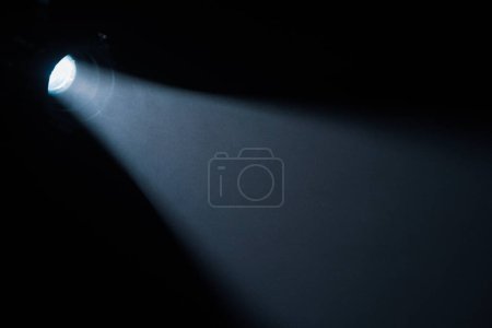 Foto de Rayos de luz del centro de atención en estudio oscuro con humo. Corriente de luz desde el foco de la película sobre fondo negro. Partículas de humo flotando en los rayos de luz - Imagen libre de derechos