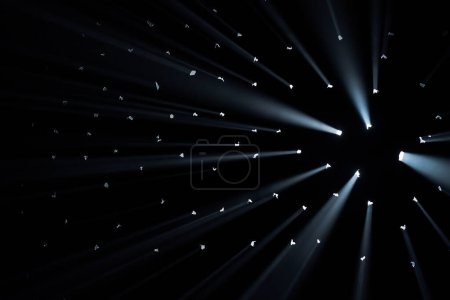 Foto de Los rayos de luz brillante atraviesan agujeros en el fondo negro del estudio. Los rayos atraviesan la oscuridad iluminando el espacio - Imagen libre de derechos