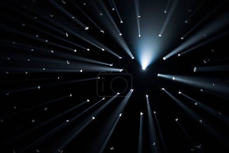 Téléchargez les photos : Des rayons de lumière brillante traversent des trous dans le fond noir du studio. Les rayons coupent à travers l'obscurité illuminant l'espace - en image libre de droit