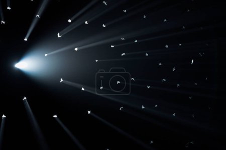 Photo for Rays of bright light come through holes in the black background of the studio. The rays cut through the darkness illuminating the space - Royalty Free Image
