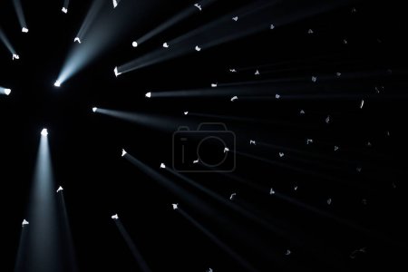 Photo for Rays of bright light come through holes in the black background of the studio. The rays cut through the darkness illuminating the space - Royalty Free Image