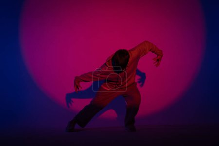 Foto de Tipo con ropa casual bailando elementos de hip hop en estudio con luz azul. La bailarina está en el círculo rojo del centro de atención y demuestra la plasticidad corporal. A toda altura. Coreografía callejera moderna - Imagen libre de derechos