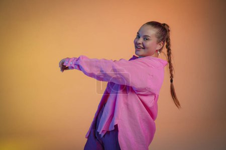 Foto de Una joven con una camisa rosa posa sobre un fondo de estudio naranja. La bailarina muestra elementos de la coreografía jazz-funk. Coreografía moderna - Imagen libre de derechos