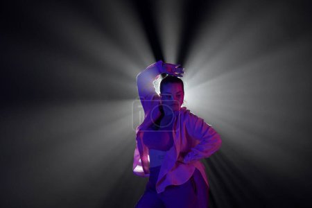 Photo for Girl in pink clothes dancing in dark studio with smoke and backlight. The dancer demonstrates elements of choreography in jazz funk style - Royalty Free Image