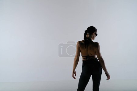 Foto de Mujer joven en negro revelando ropa posando sobre fondo de estudio blanco. La bailarina posa y muestra su cuerpo delgado. El concepto de la danza de tiro de promoción - Imagen libre de derechos