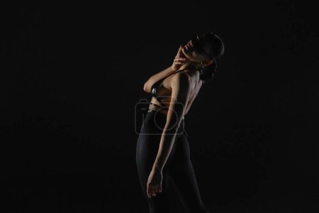 Foto de Mujer joven en corpiño negro y medias posa sobre fondo negro estudio retroiluminado. Bailarina femenina demuestra elementos de danza en tacones altos. Danza concepto de vídeo promocional - Imagen libre de derechos