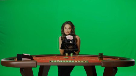 Photo for Casino and gambling commercial advertisement concept. Elegant female in studio on chroma key green screen. Attractive woman in black dress at the blackjack poker table holding fan of cards. - Royalty Free Image