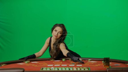 Photo for Casino and gambling commercial advertisement concept. Female in studio on chroma key green screen close up. Woman in black dress at the blackjack poker table pointing at the cards. - Royalty Free Image